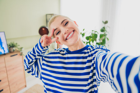 Charming young woman enjoying leisure time in stylish living room, wearing casual striped pulloverの写真素材