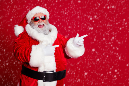 Photo of funny man direct finger empty space wear santa hat costume isolated red color backgroundの写真素材