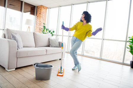 Young woman cleaning and dancing in a stylish living room, enjoying a bright day indoors, wearing casual fashionの写真素材