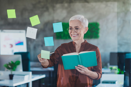 Photo of professional mature lady corporate leader write notebook business strategy stickers ideas wear brown shirt coworking light officeの写真素材