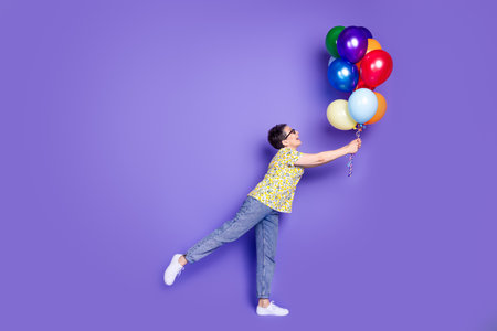 Elderly woman with colorful balloons on violet background, expressing joy and energyの写真素材