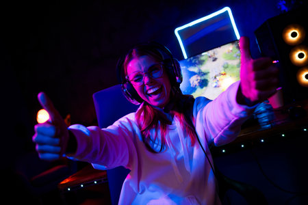 Photo of gamer lovely blonde young lady excited thumb up approve play strategy game late night room indoors purple blue neon lightの写真素材