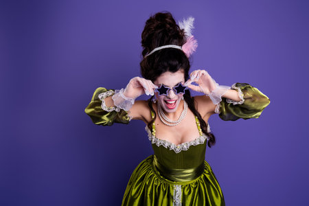 Elegant woman in green historical dress posing with star glasses against a purple background showcasing a blend of classic and modern themesの写真素材