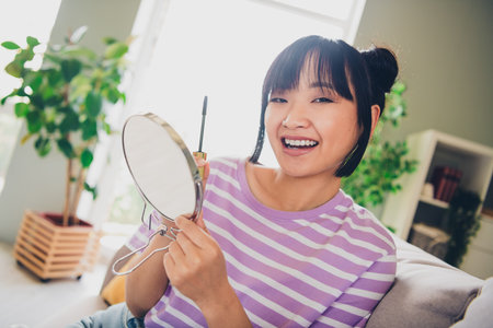 Photo of adorable sweet lady wear violet striped t-shirt applying mascara indoors room home houseの写真素材