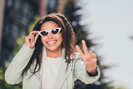 Young woman enjoying sunny day outdoors in the city wearing stylish sunglasses and a trendy coatの写真素材