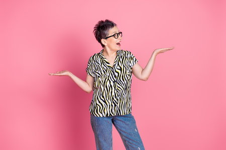 Portrait of pretty aged lady look hold empty space scales wear zebra print shirt isolated on pink color backgroundの写真素材