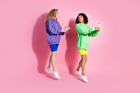 Two stylish women in colorful outfits enjoying a fun moment together against a vibrant pink...