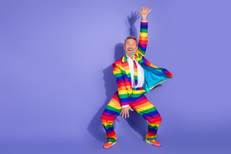 Vibrant elderly man in rainbow suit exuding joy and charisma on a purple background at a disco partyの写真素材