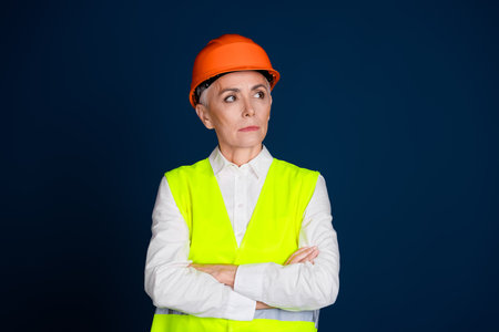 Confident senior woman in construction uniform with hardhat against dark blue background, showcasing...