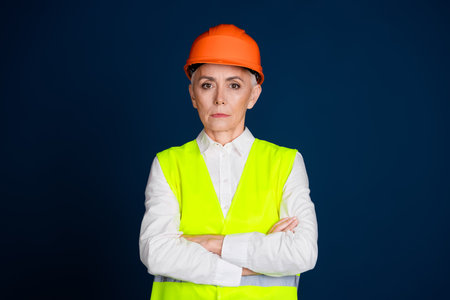 Confident mature woman in safety gear standing against dark blue background, representing professionalismの写真素材