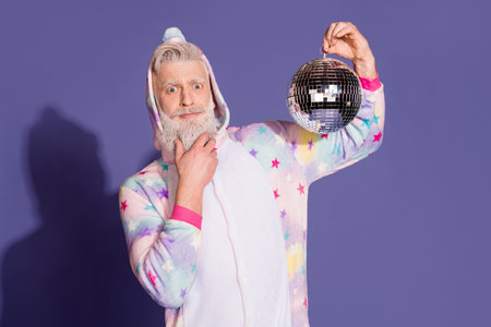 Cheerful mature man in unicorn pajama holding a disco ball against a purple backgroundの写真素材