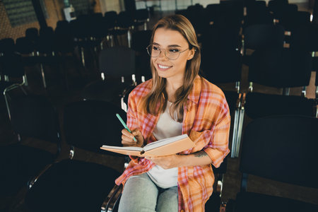 Photo of pretty young blonde girl listen write notebook wear plaid shirt coworking college auditorium listen speaker light interior indoorの写真素材
