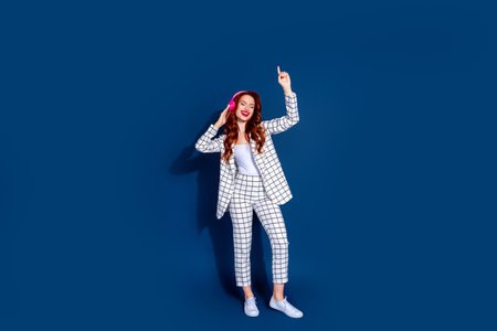 A young fashionable woman with red hair and bright lipstick joyfully dances against a dark blue background, showcasing eleganceの写真素材