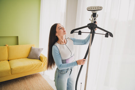 Young woman using a garment steamer in a modern home interior, enjoying a relaxed moment amid a colorful and stylish living room settingの写真素材