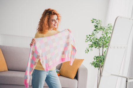 Photo of positive good mood woman dressed yellow sweater trying on new pullover indoors house apartment roomの写真素材