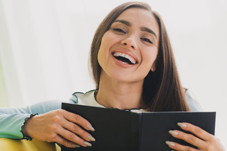 Young smiling woman reading a book at home with bright natural light enjoying a peaceful indoor momentの写真素材