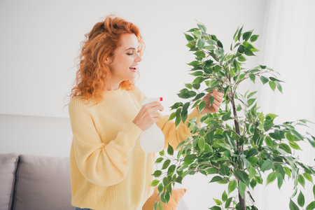 Photo of shiny cute girl dressed yellow jumper enjoying watering flower indoors house apartment roomの写真素材