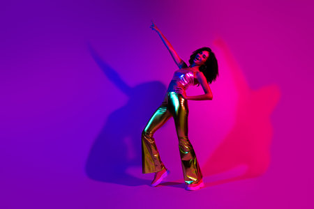 Stylish young woman dancing in neon light wearing shiny retro fashion, exuding vibrant energy and charmの写真素材