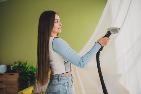Young woman steaming curtains in a cozy home interior with a modern garment steamerの写真素材