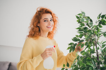 Photo of pretty cheerful lady wear yellow pullover enjoying housekeeping watering flower indoors room home houseの写真素材