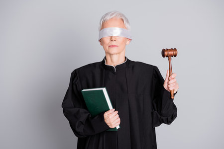 Photo of old woman judge with closed eyes hold book raise gavel isolated grey color backgroundの写真素材
