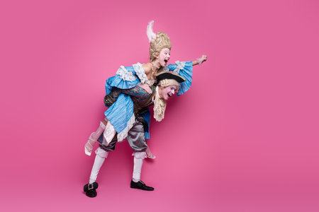 Festive duo dressed in colorful baroque costumes joyfully posing against a vibrant pink backdrop, embracing the spirit of a funの写真素材