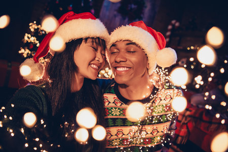 Portrait of two young people couple closed eyes fairy time celebrate xmas new year garland lights flat indoorsの写真素材