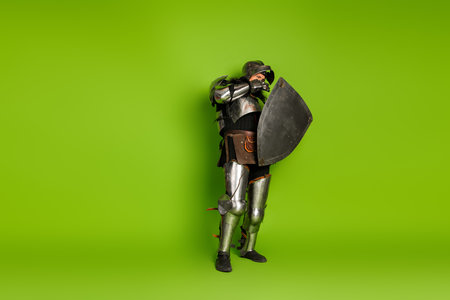 Medieval knight in full armor holding a shield, standing confidently against a vibrant green backdrop embodying historical fantasy.の写真素材