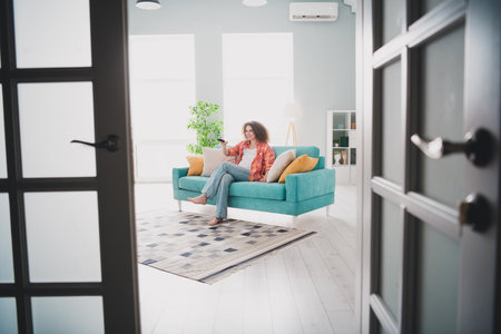 Young woman relaxing on a sofa in a bright living room with indoor plants and modern decor during a light-filled day at homeの写真素材