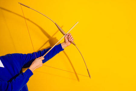 Close-up of a hand using a wooden bow against a vibrant yellow background