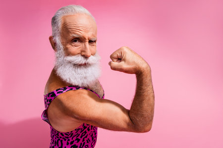 Photo of positive cheerful strong man wear stylish print clothes showing muscles isolated on pink color backgroundの写真素材