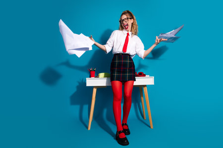 Dynamic young woman celebrating while tossing papers in vibrant blue settingの写真素材