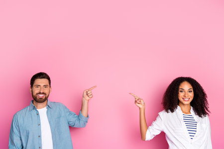 Happy couple on pink background pointing to space, smiling and enjoying their casual dayの写真素材
