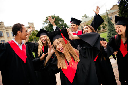 Joyful college graduates celebrating together outdoors on a vibrant summer day, expressing happiness and accomplishment.の写真素材
