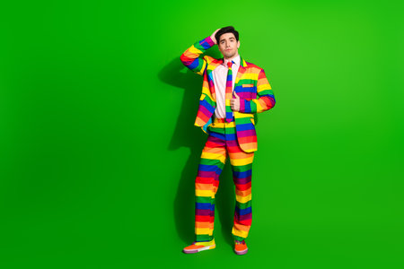 Young man in a colorful rainbow-striped suit standing against a vivid green background with a confident poseの写真素材