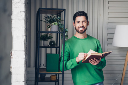 Casual man reading a book at home, standing in a cozy interior with stylish decor and natural daylightの写真素材