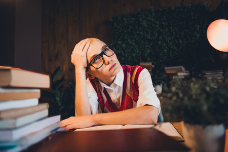 Young woman in a stylish argyle waistcoat and glasses studying indoors, surrounded by books.