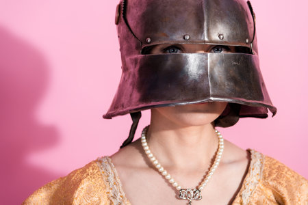 Woman in medieval steel helmet with pearl necklace and elegant attire against vibrant pink...
