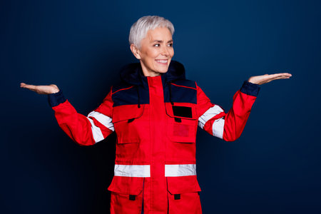 Photo of nice senior woman compare hold empty space wear uniform paramedic doctor help isolated on dark blue color backgroundの写真素材