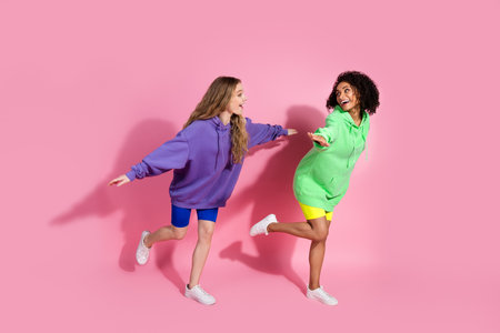 Two young women posing playfully in colorful casual hoodies, pink background emphasizing friendship and joyの写真素材