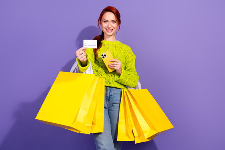 Cheerful woman holding yellow shopping bags and a card against a vibrant purple background,...