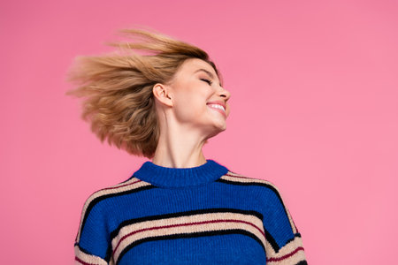 Cheerful woman in a blue striped sweater with a bob hairstyle enjoying vibrant energy against a pink backgroundの写真素材