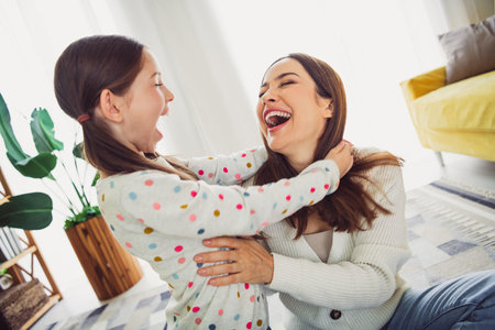 Joyful bonding moment between mother and daughter laughing together indoors, enjoying a relaxing spring day at homeの写真素材