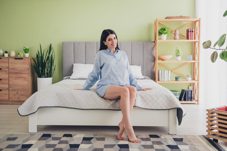 Charming young woman enjoying a peaceful morning sitting on bed in stylish bedroom wearing blue pajamasの写真素材