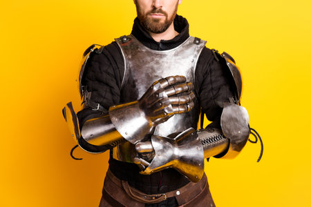 Medieval knight in shining armor posing against bright yellow background, showcasing traditional historical costumeの写真素材