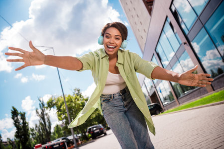 Joyful young woman with headphones reaching out on a sunny city streetの写真素材