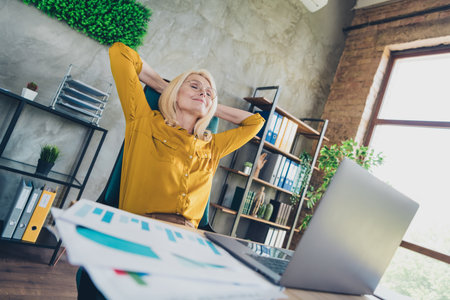 Photo of sweet charming lady assistant wear shirt finish work modern gadget arms behind head indoors workplace workstationの写真素材