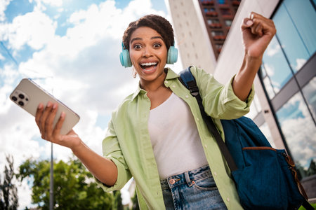 Joyful woman listening to music on headphones while holding smartphone outdoorsの写真素材