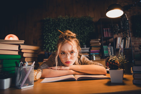 Young woman studying late at night, surrounded by books, looking thoughtful and curious in a cozy home office setting with natural light.の写真素材