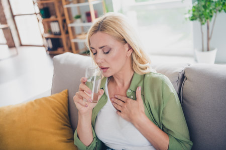 Middle-aged woman enjoying a calm moment at home with a glass of water, wearing a casual shirt